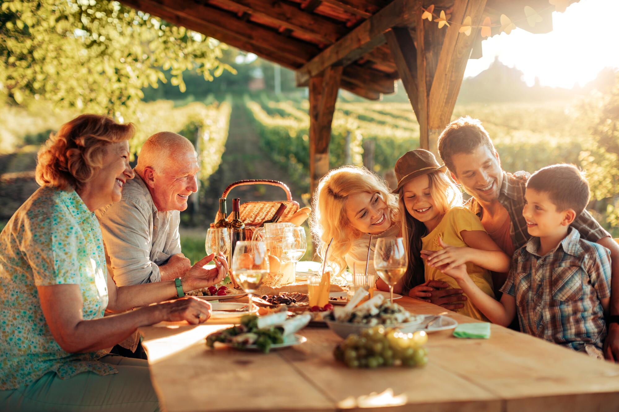 a multi-generational family sitting at a long table at a vineyard estate, passing bread and wine 